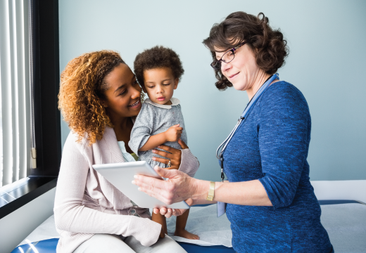 Photo of a pediatrician showing a digital tablet to a parent holding their toddler