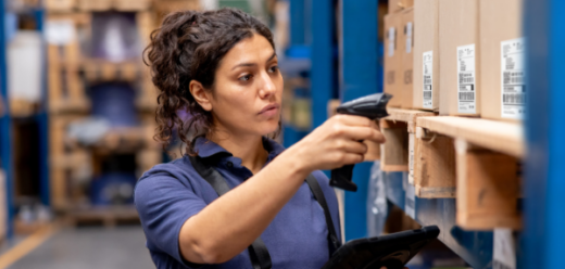 Photo of a worker at a distribution warehouse taking inventory using a bar code reader and a tablet.