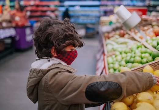 Young boy wearing a mask chooses fruit in a grocery store.