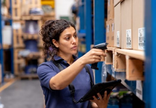 Photo of a worker at a distribution warehouse taking inventory using a bar code reader and a tablet.