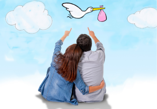 Photo of a seated couple pointing at the image of a stork carrying a pink bundle.